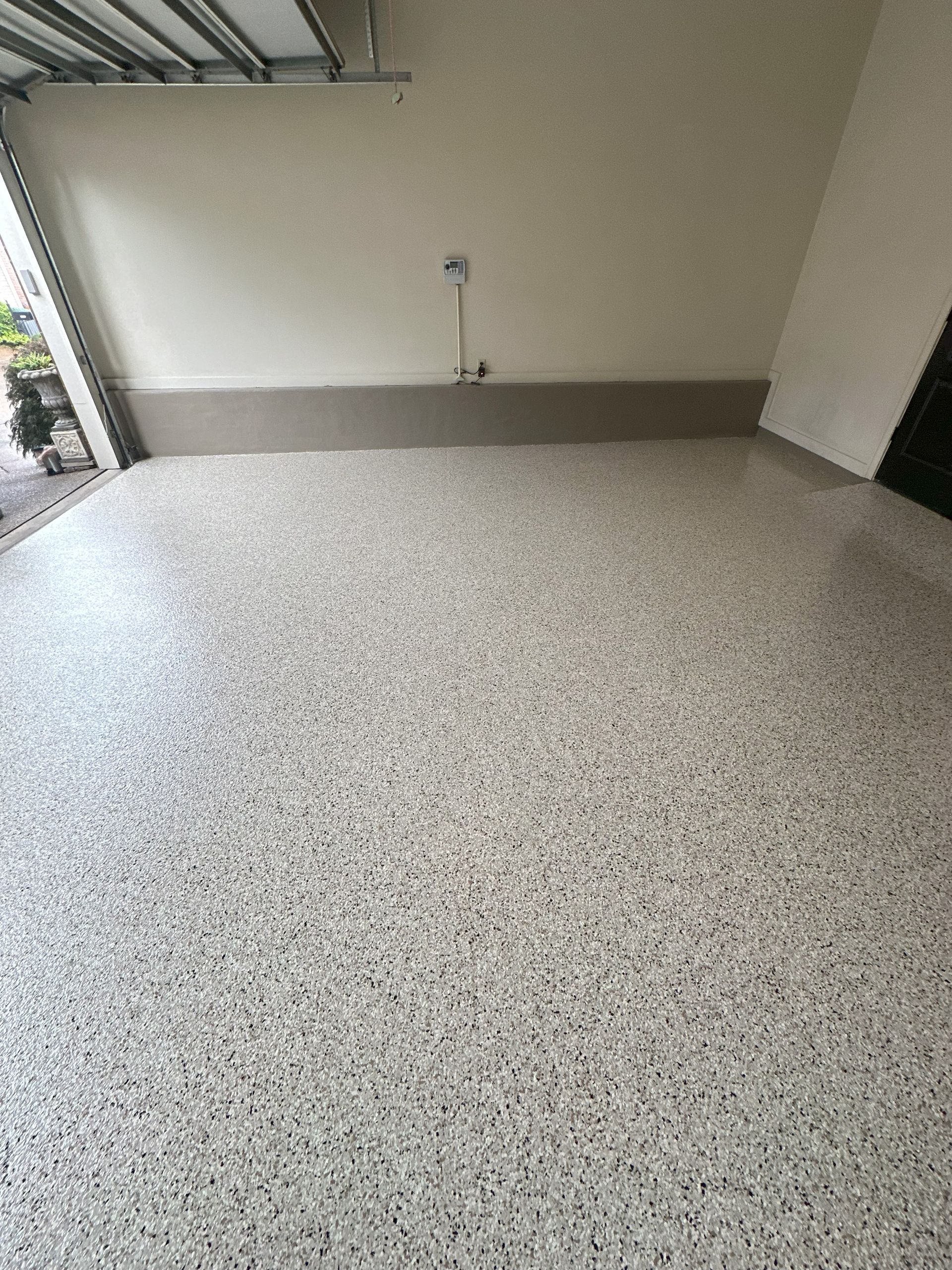 Garage interior with speckled epoxy floor, beige walls, and open garage door.