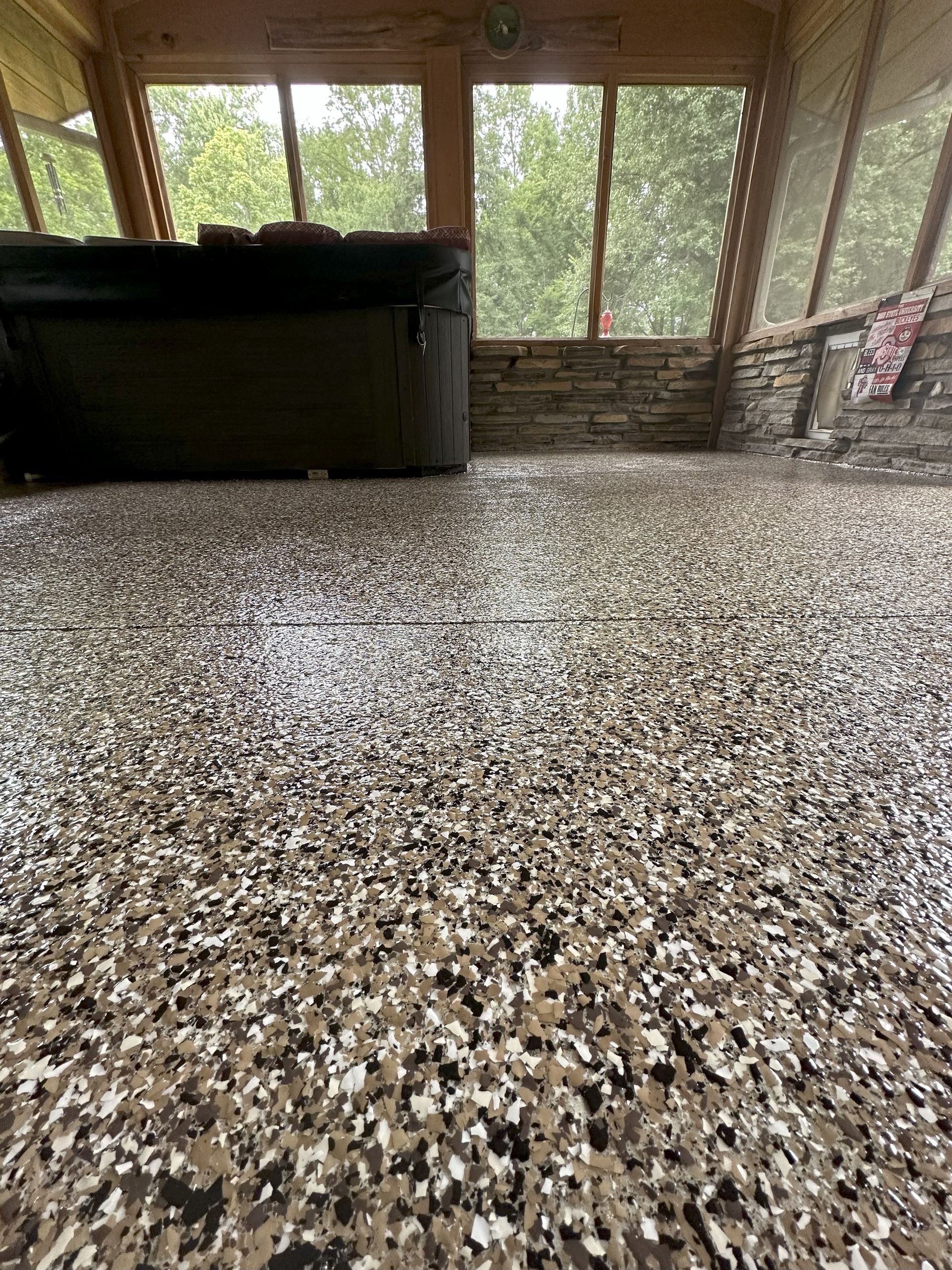 Epoxy-coated floor in a screened-in porch with a hot tub and windows looking out onto trees.