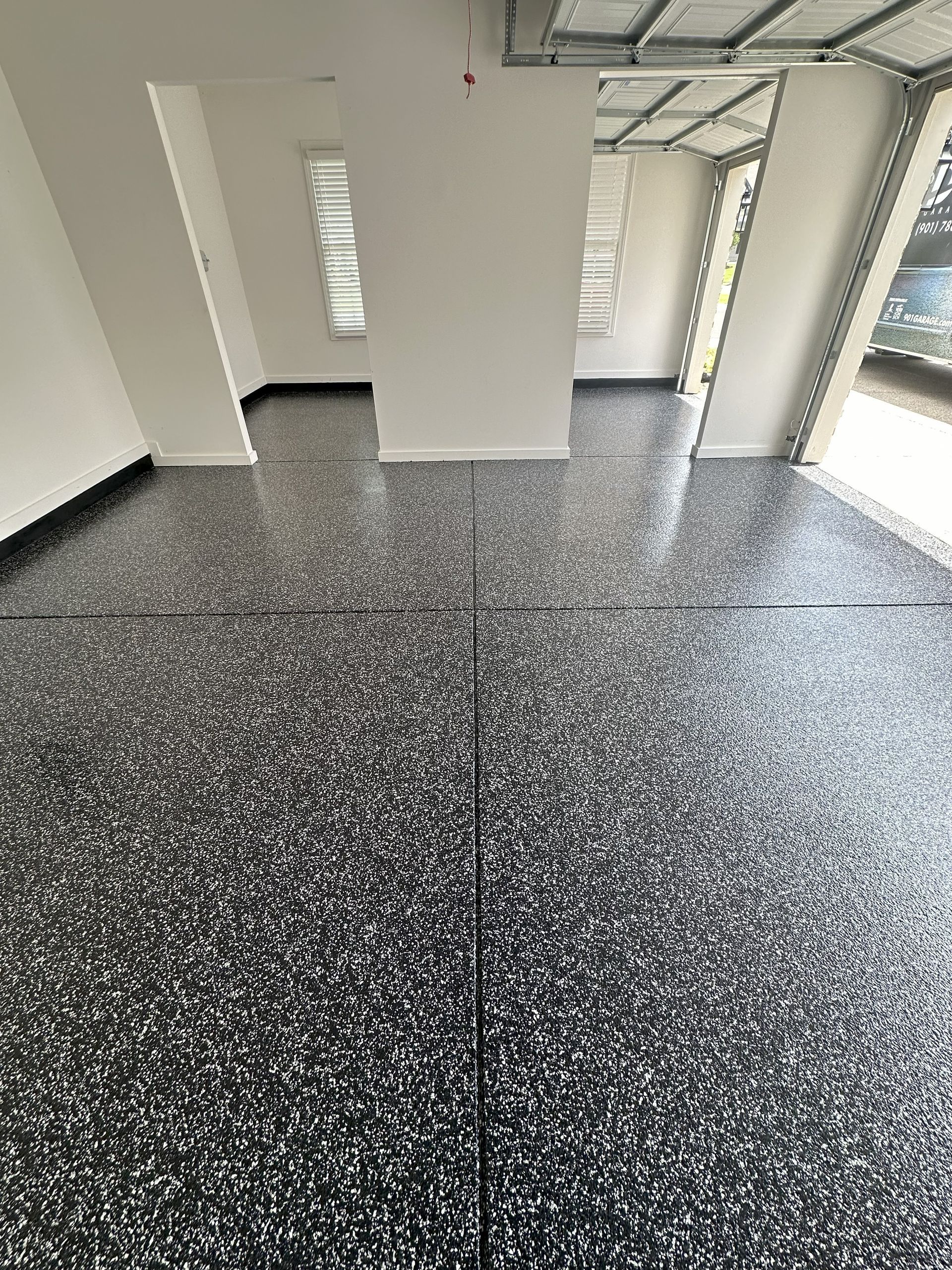 Black and white speckled floor in a room with white walls, window and doorways; construction in progress.