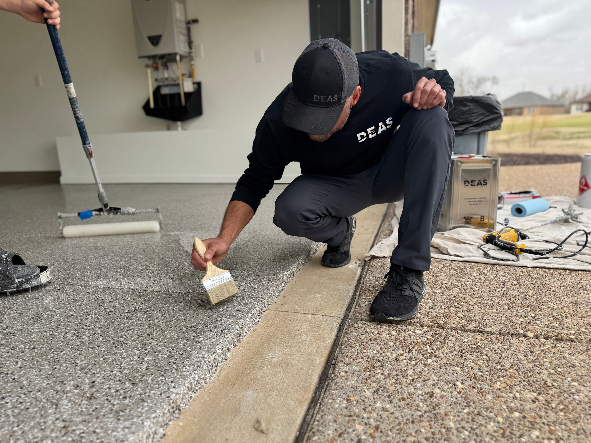 Worker applying sealant to a concrete seam on a rooftop, with tools nearby.