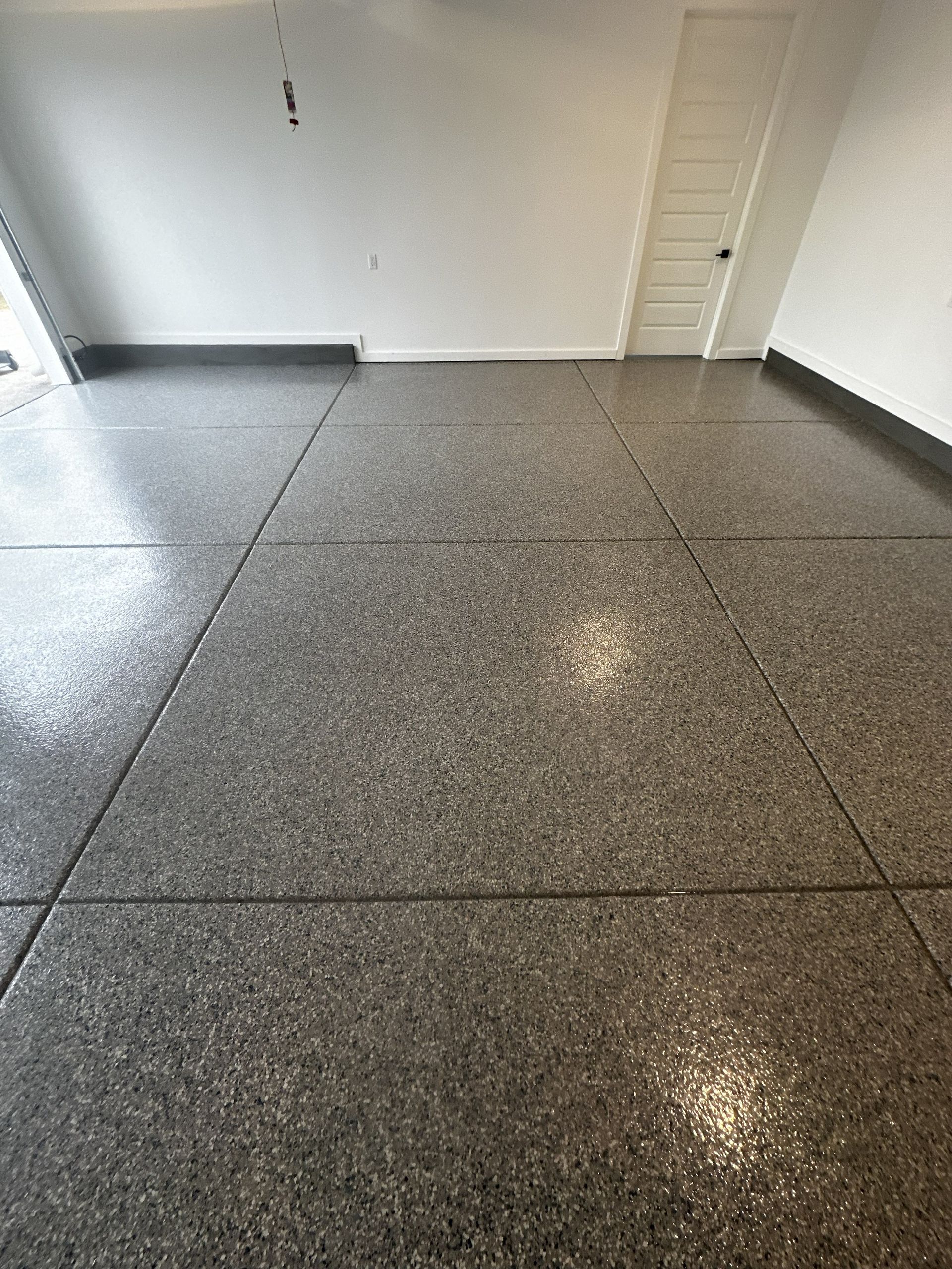 Garage floor with gray speckled epoxy coating, bordered by black. White walls and door.