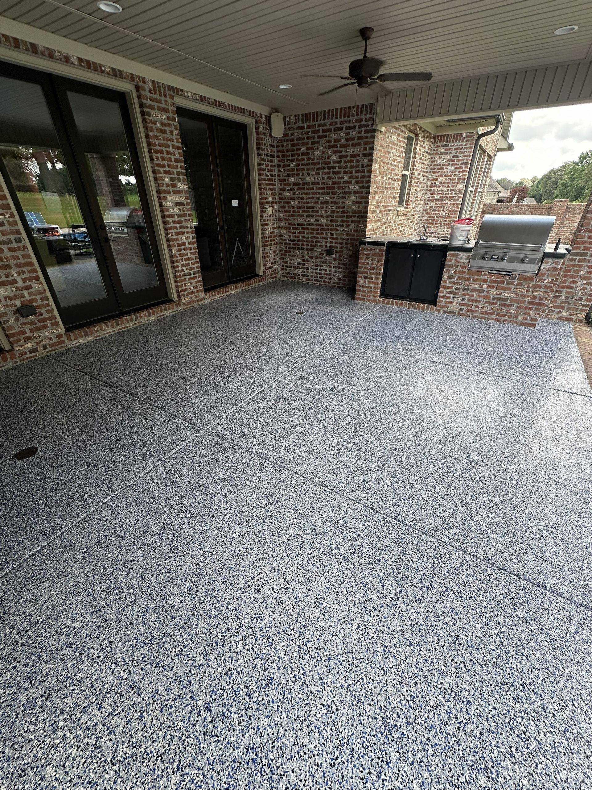 Outdoor patio with speckled flooring, brick walls, and a built-in grill area.