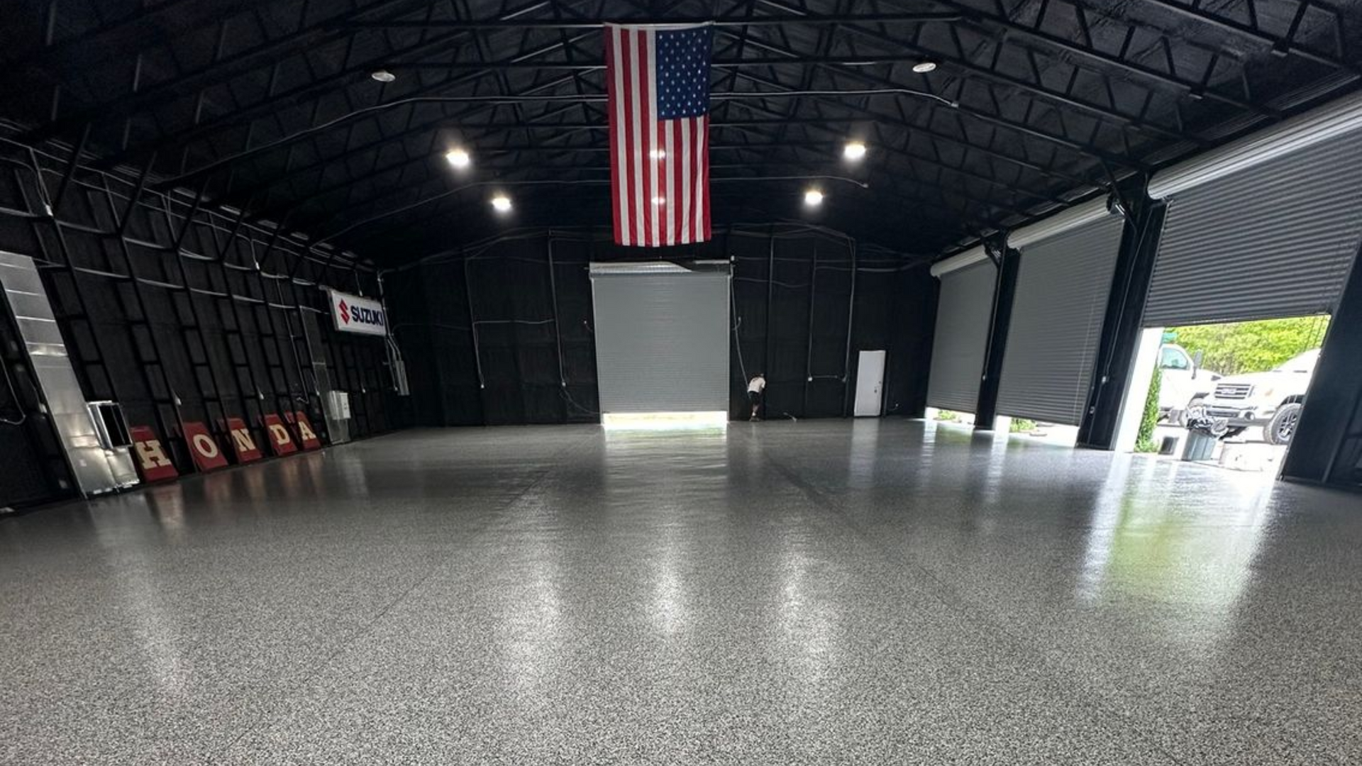 Large, empty warehouse with shiny gray floor and open door, American flag hanging from ceiling.