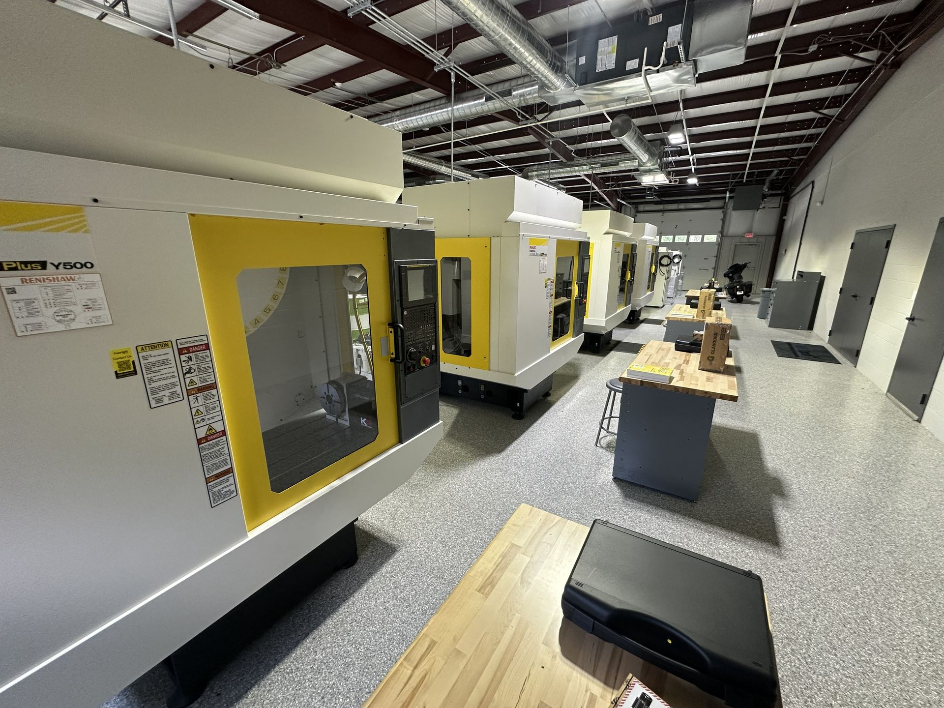 Machining shop interior with several white and yellow CNC machines in a row.