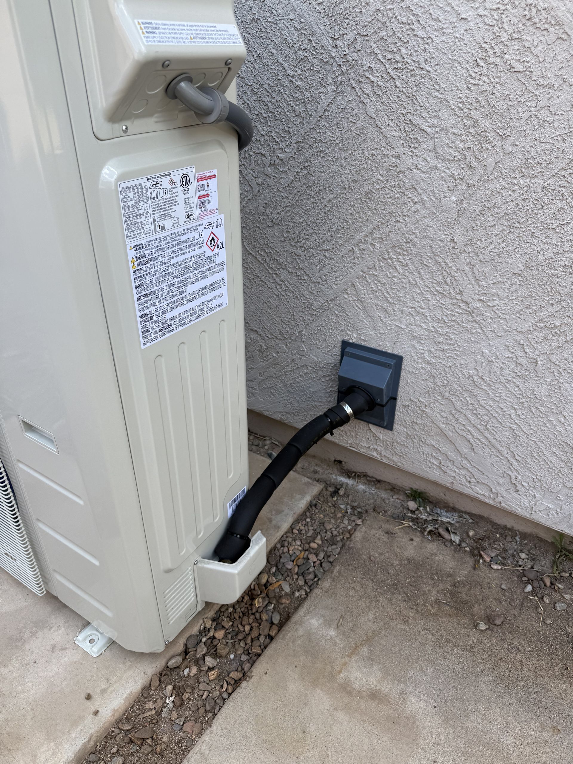 Black cable from outdoor electrical box to wall outlet beside a stucco wall and concrete walkway