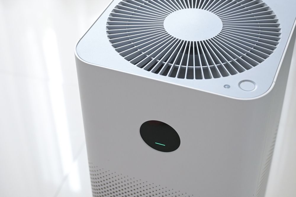 White air purifier with circular top vent and small display, standing by a bright window