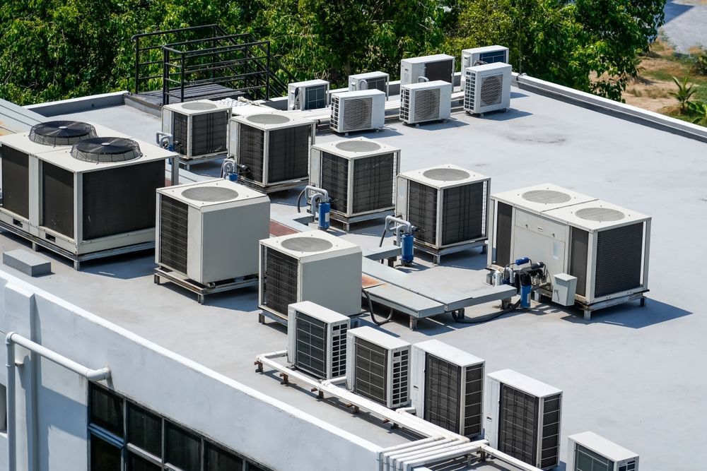 Rooftop with multiple HVAC units and ventilation equipment in sunlight, surrounded by trees
