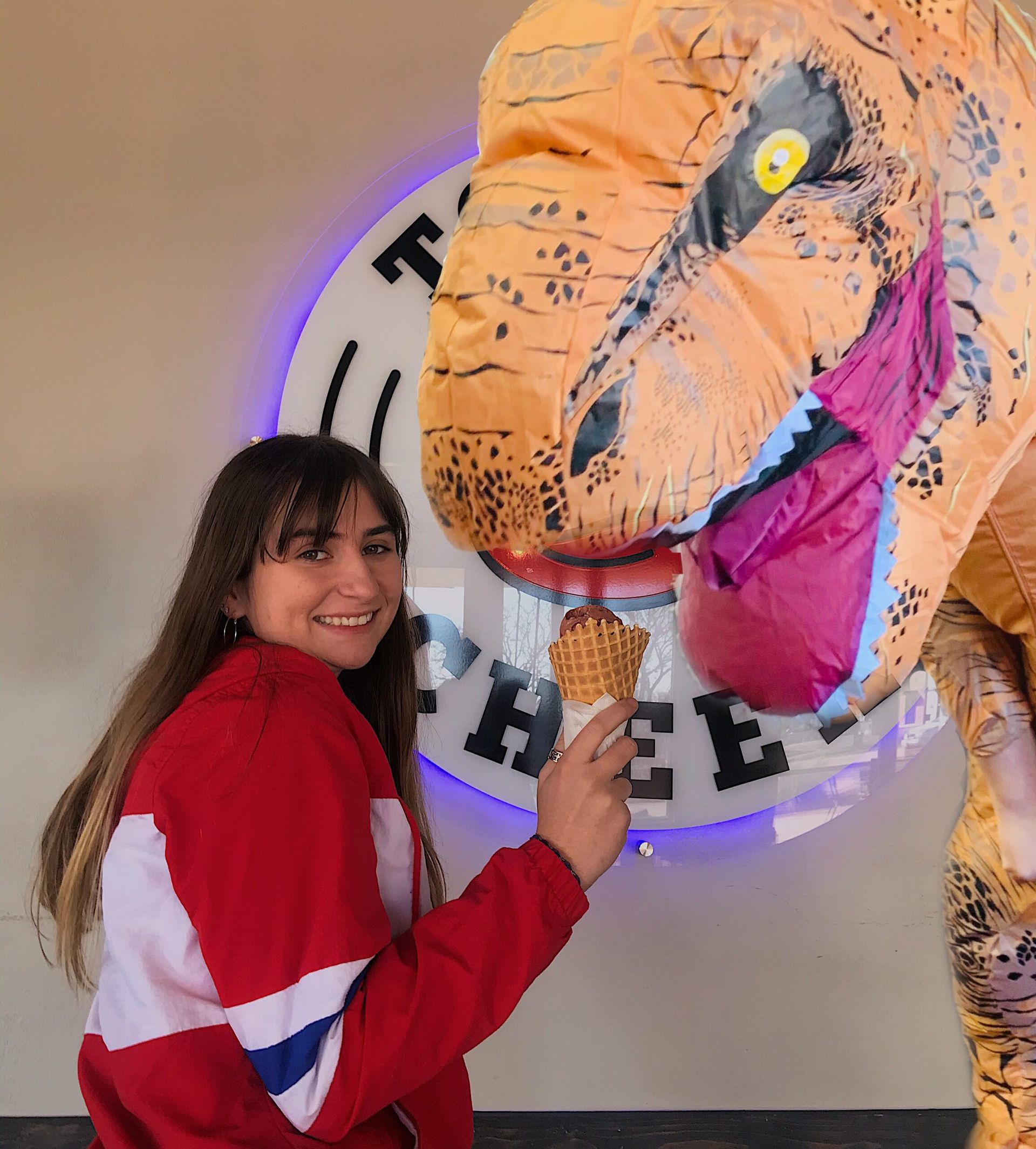 A girl in a red jacket is standing next to a t-rex costume