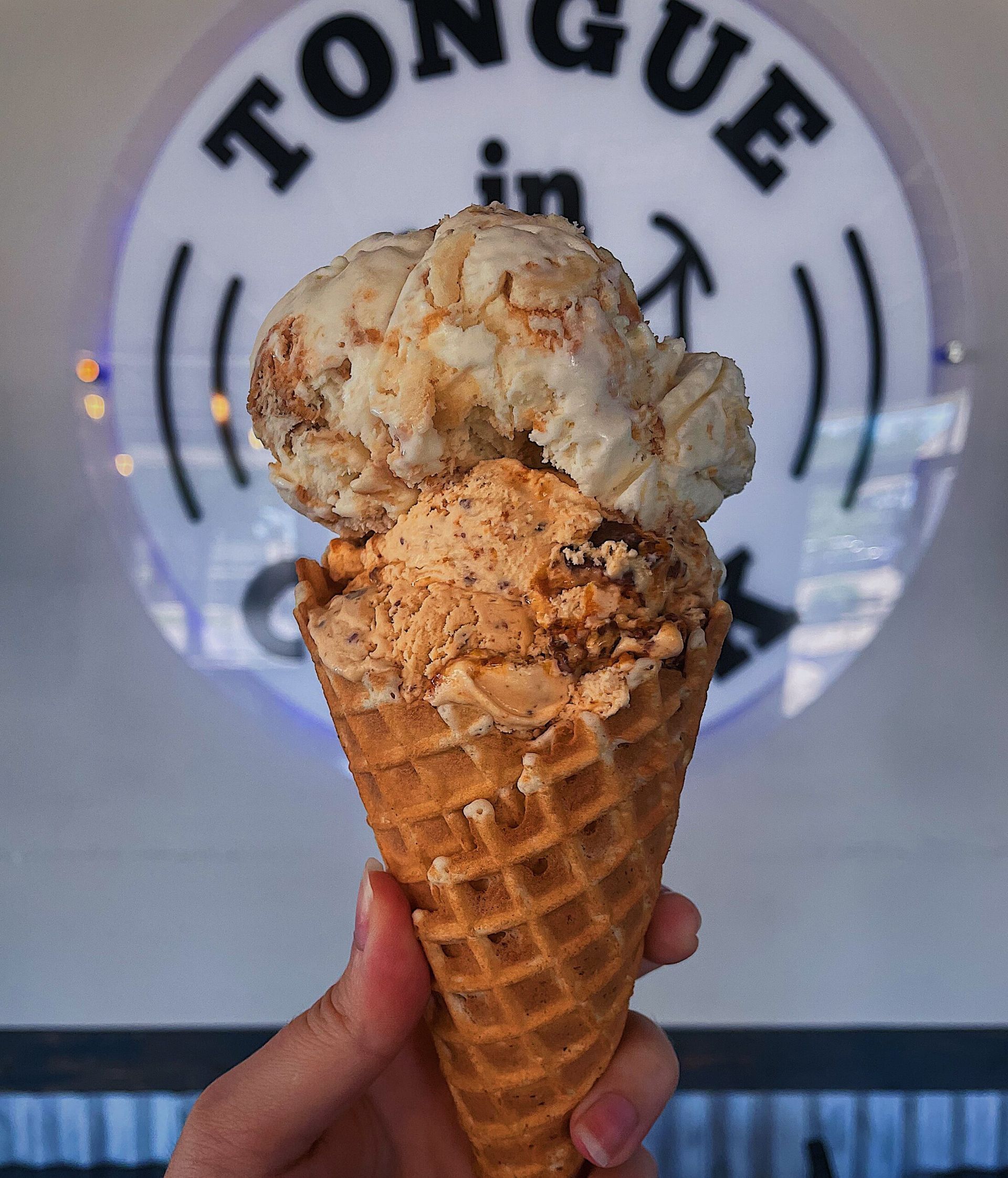 A person is holding an ice cream cone in front of a sign that says tongue in a circle