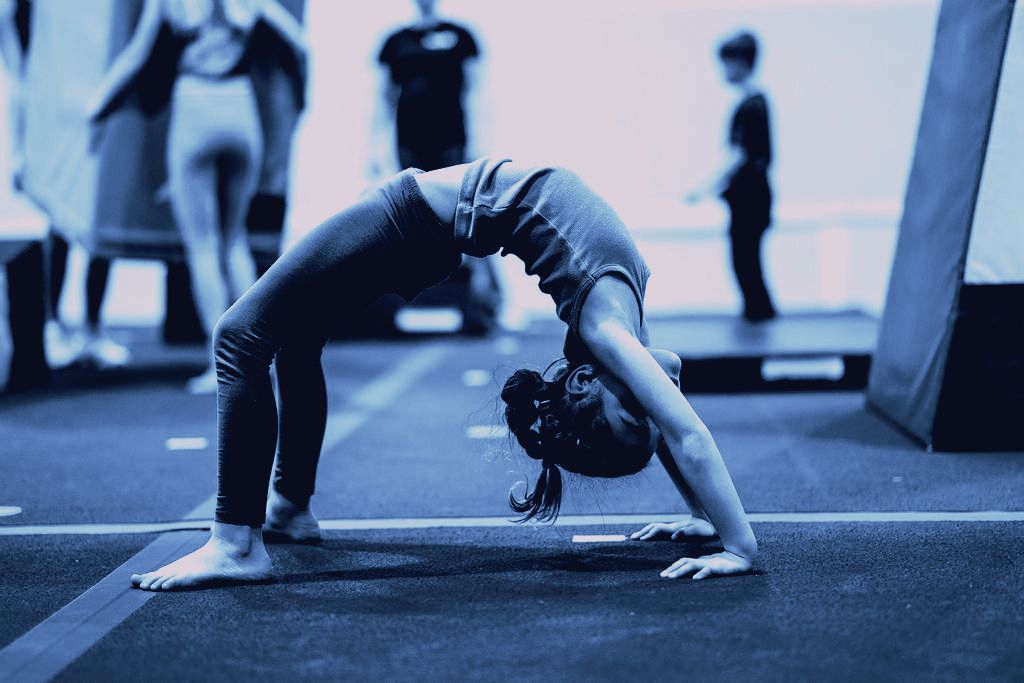 A young girl is doing a handstand on a gym floor.