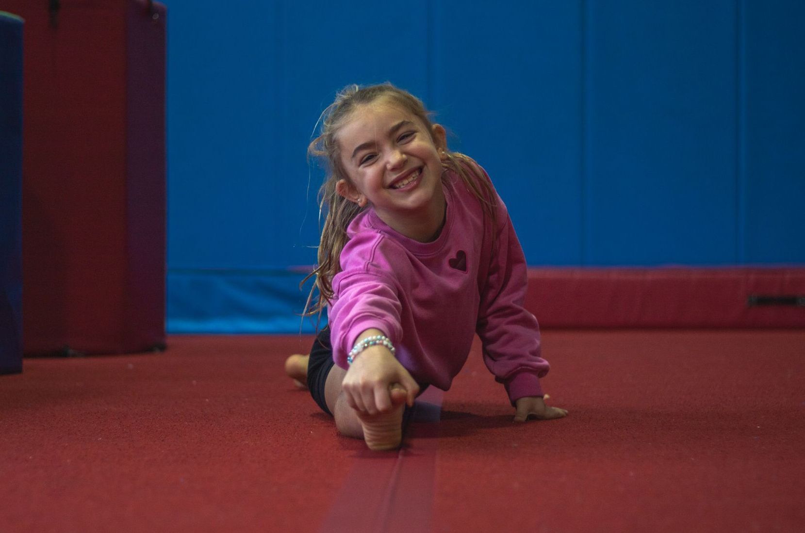 A little girl is doing a split on a blue mat