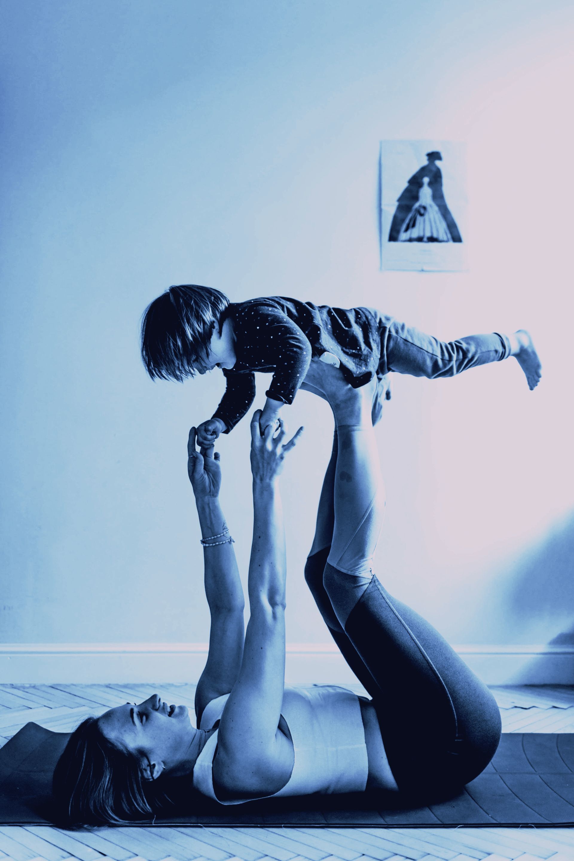 A woman is laying on a yoga mat holding a child in her arms.