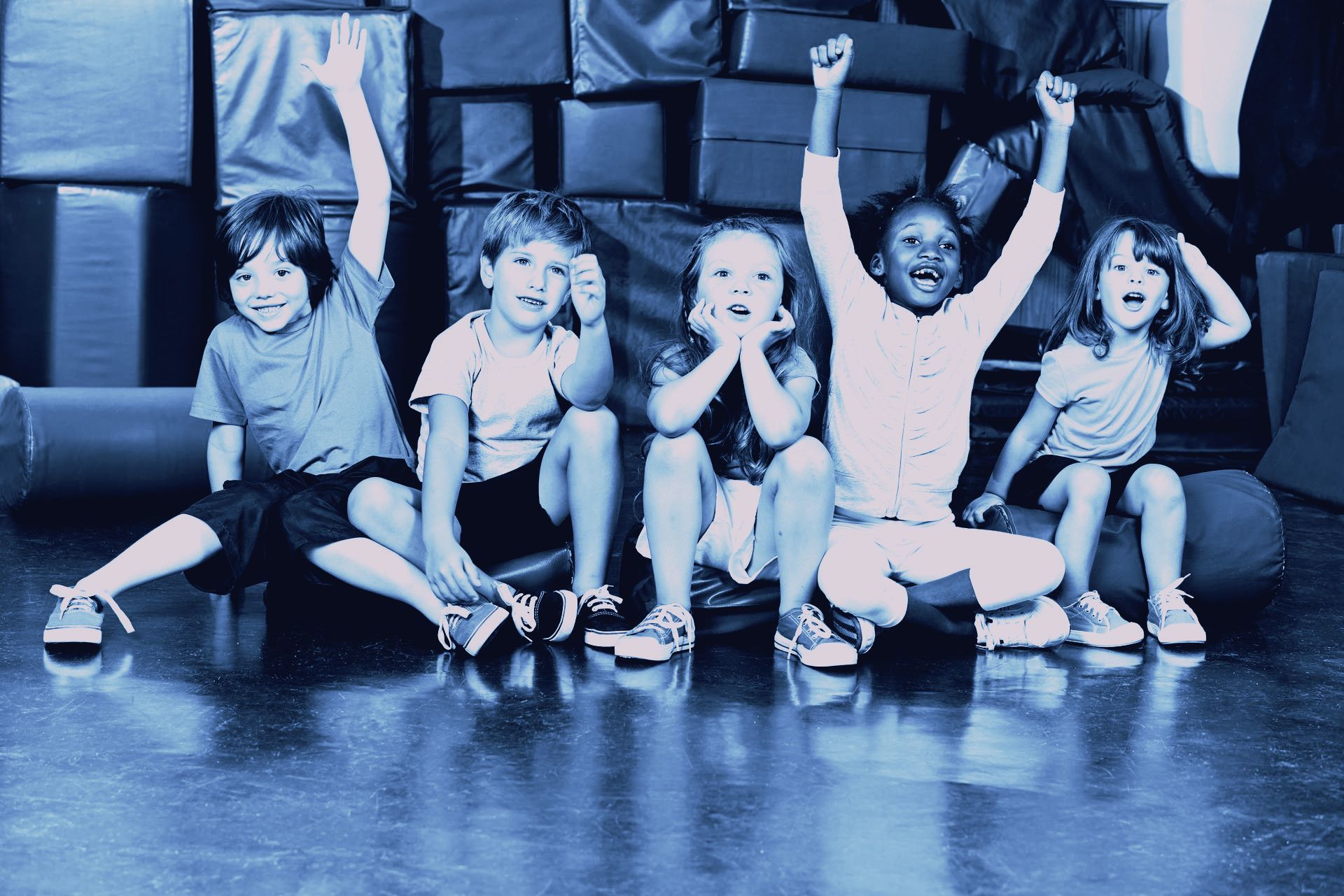A group of children are sitting on the floor with their arms in the air