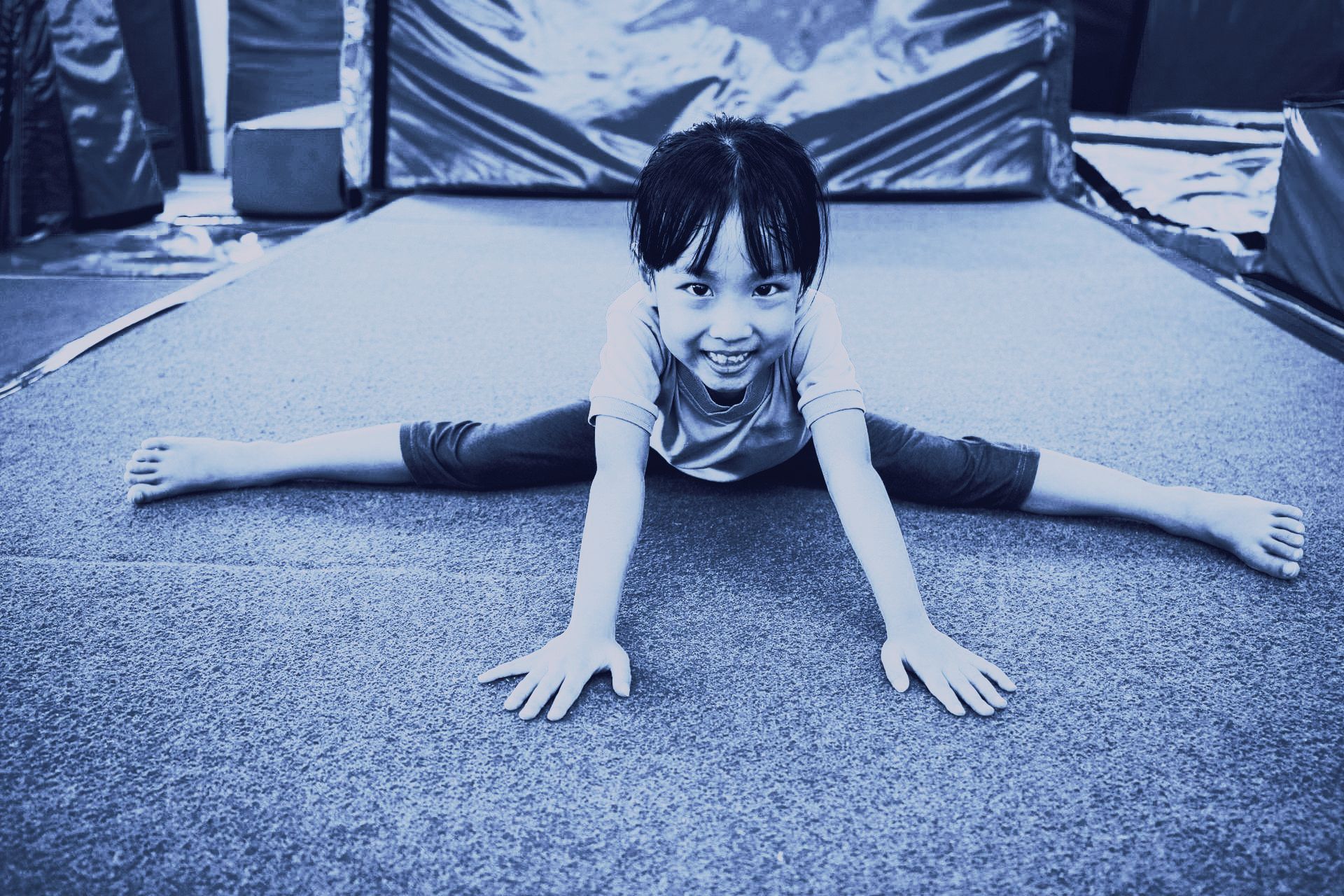 A little girl is doing a split on the floor.