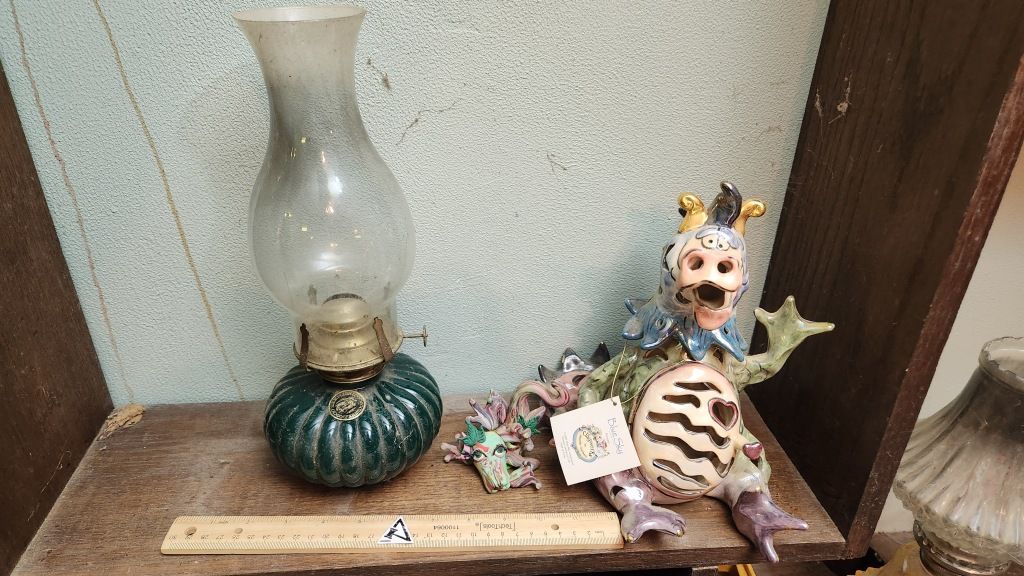 Decorative shelf with a glass lamp, green jar, ceramic cat figurine, and small ornaments on a wooden ledge