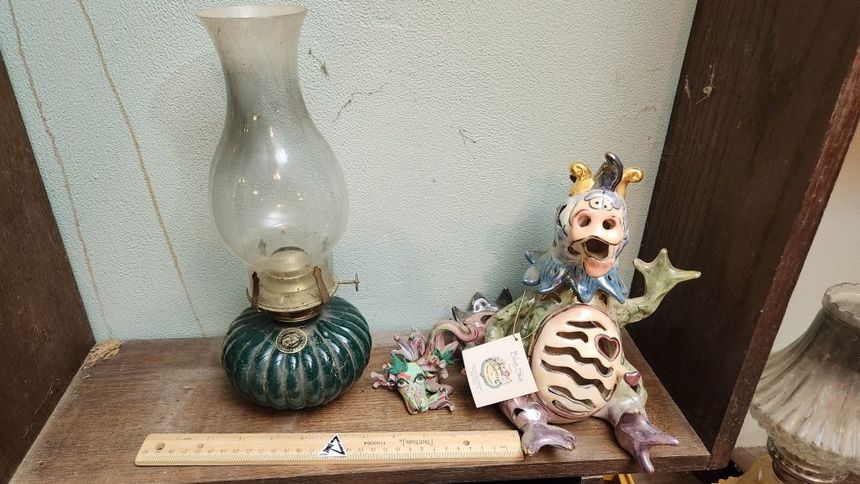 Decorative shelf with a glass lamp, green jar, ceramic cat figurine, and small ornaments on a wooden ledge