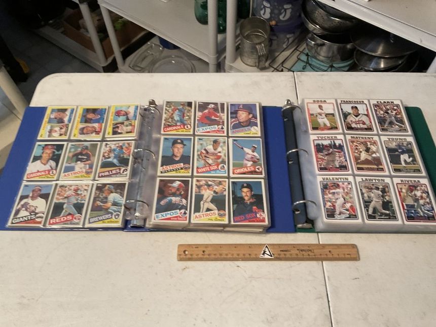 Open binder of colorful trading cards on a table, with a ruler in front and another card binder to the side