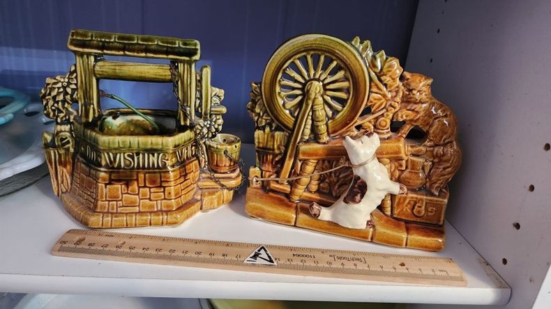 Two small decorative wooden water wheel scenes on a store shelf, one with a bench and one with a cat figurine.