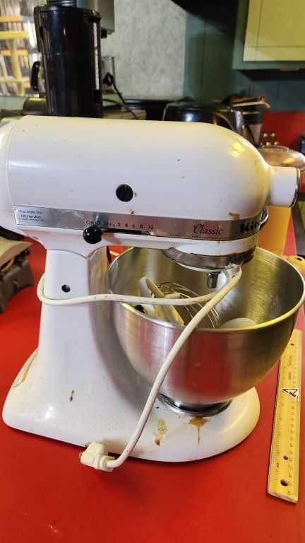White stand mixer with stainless bowl on a countertop, with a measuring tape beside it.