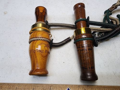 Two wooden whistles tied together with a cord, one light brown and one dark brown, on a white background