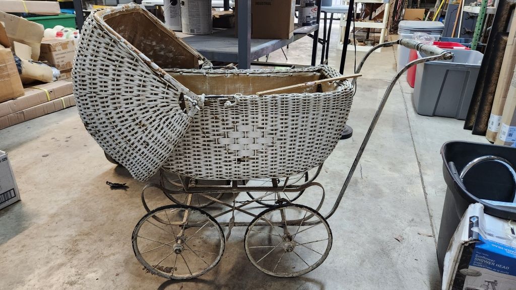 Vintage wicker baby carriage with large wire wheels in a workshop or storage area