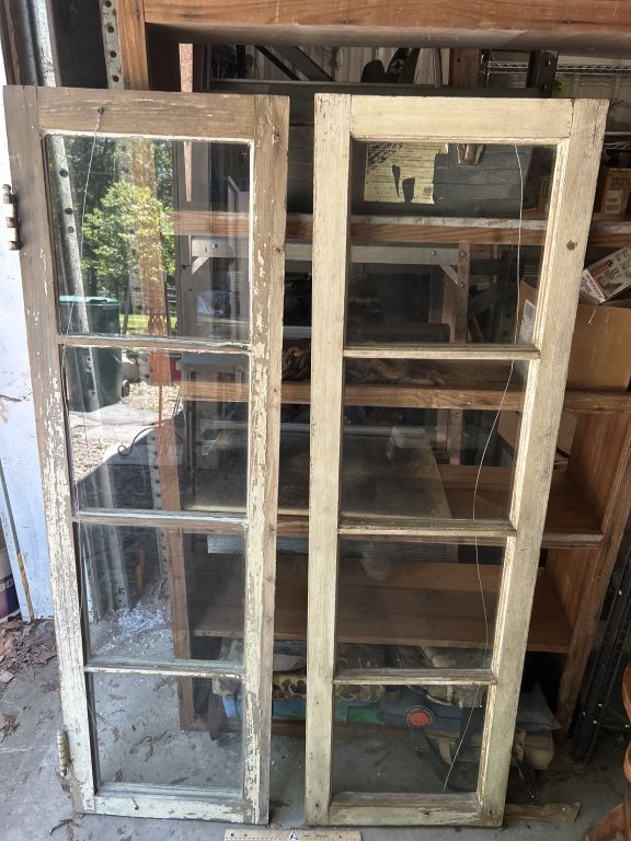 Two weathered wooden window frames with multiple panes leaning against a wall outdoors.