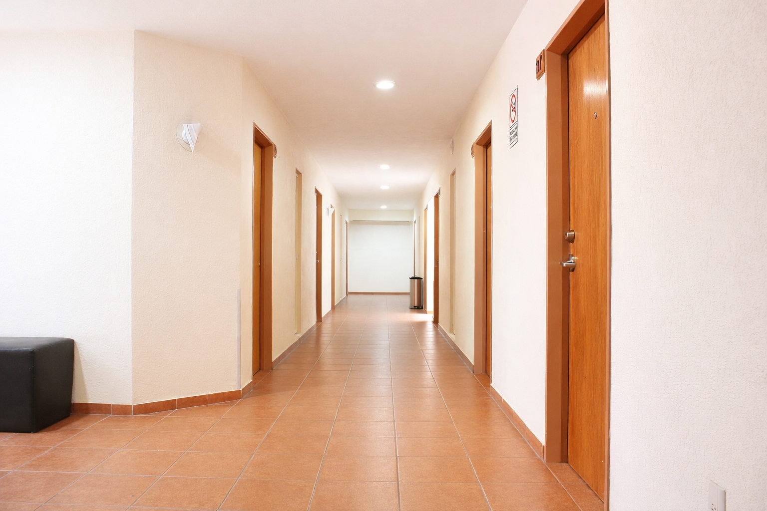 Pasillo con puertas marrones y suelo de baldosas, que conduce a una pared blanca al final.