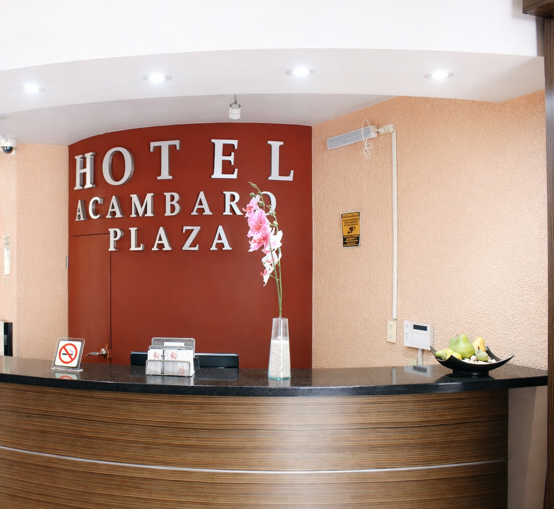 Mostrador de recepción del Hotel Cambaro Plaza con logo, flores y frutas.