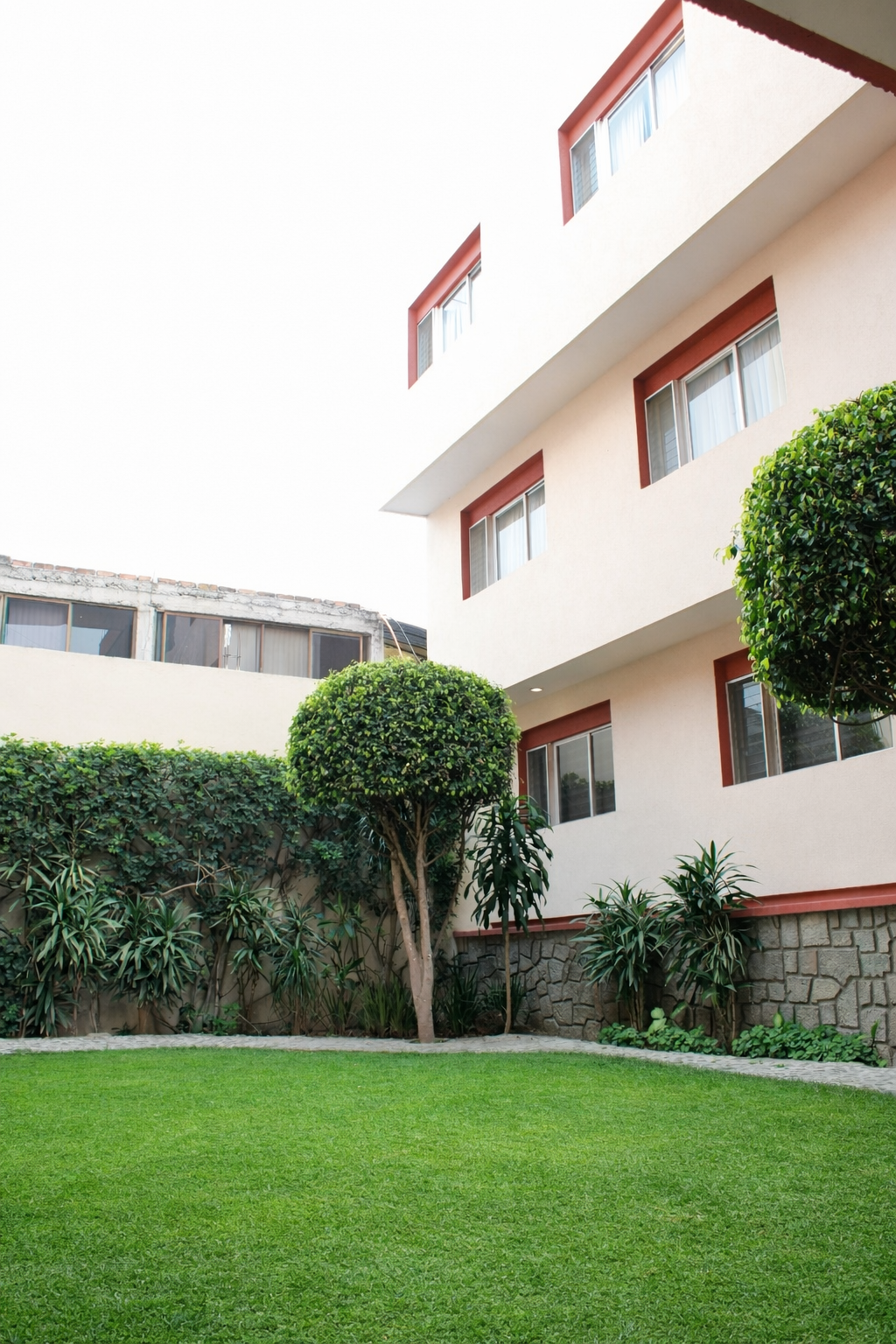 Césped verde exuberante con arbustos recortados y un edificio beige con detalles rojos.