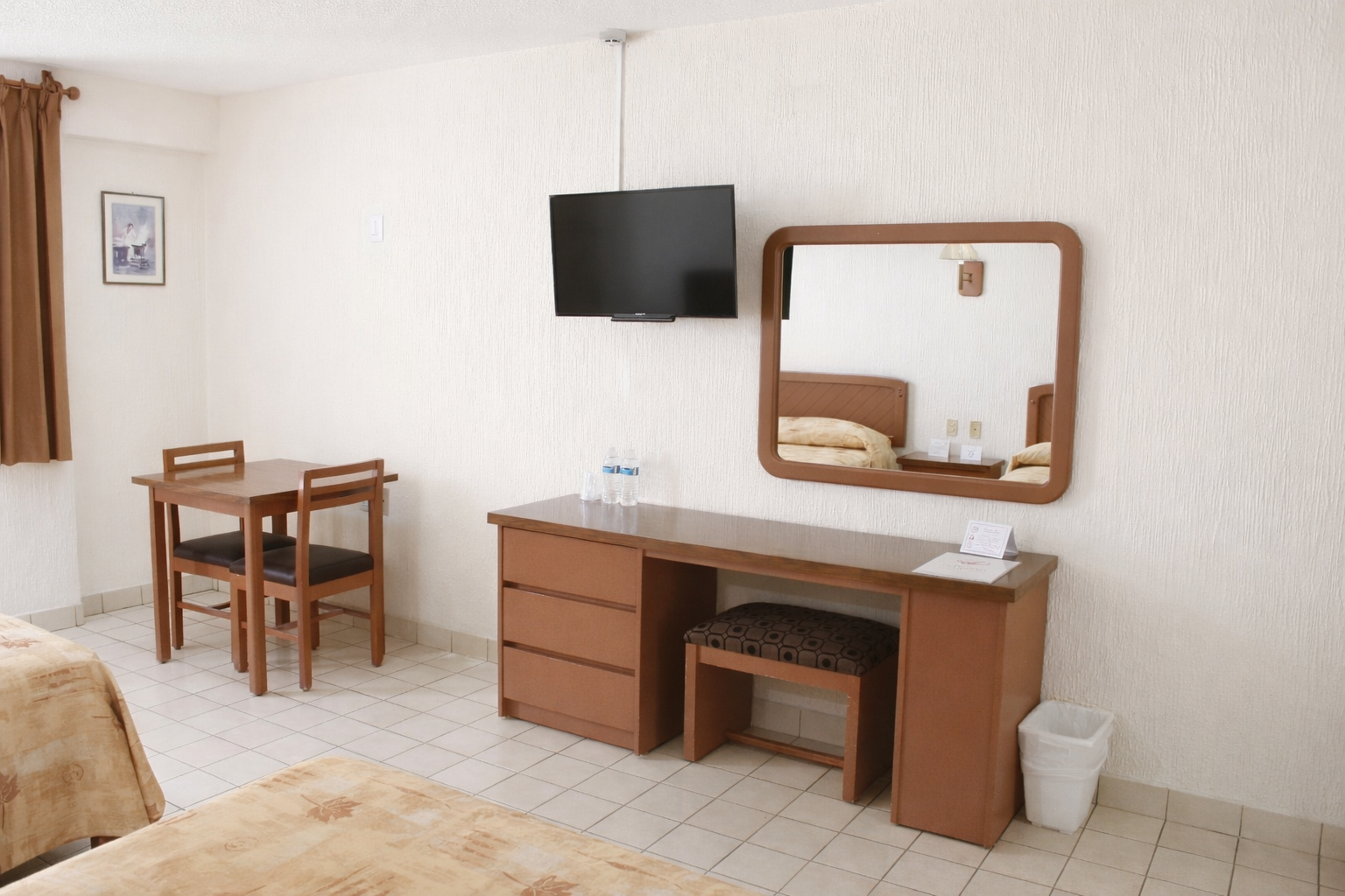 Habitación de hotel con dos camas, escritorio, espejo y una pequeña mesa con sillas.