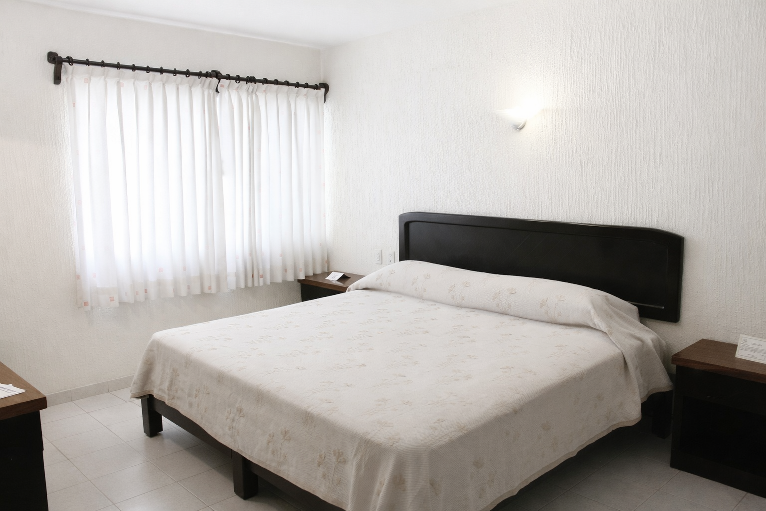 Dos camas en una habitación de hotel, con cabeceros marrones y colchas estampadas. Cortinas marrones y paredes texturizadas.