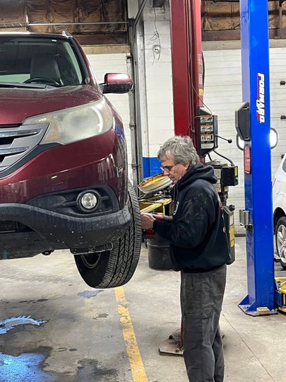 Worker inspecting a maroon SUV on a lift inside an auto repair shop | Diamond Automotive