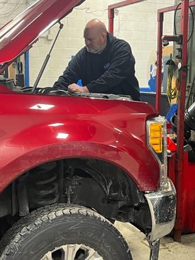 Mechanic working under the hood of a red truck in a garage | Diamond Automotive