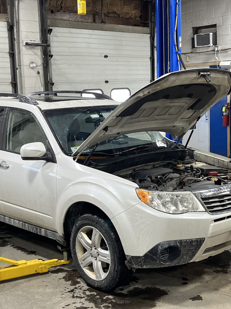 White SUV with hood open in an auto repair shop, showing engine bay on a lift | Diamond Automotive