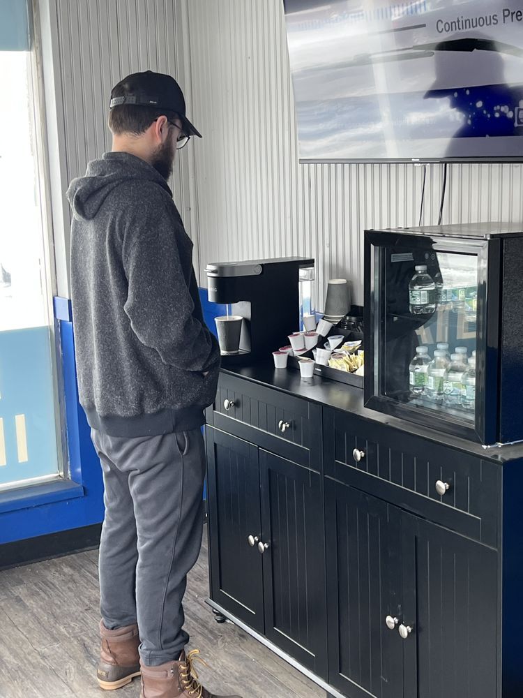 Man in a gray hoodie using a coffee station beside a black cabinet and glass display case | Diamond Automotive