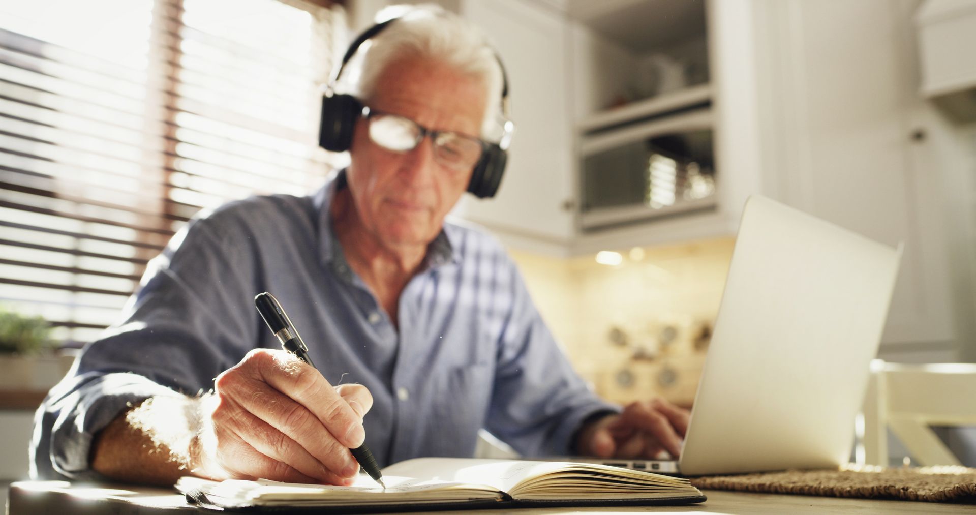 Man writing at a desk beside a laptop in a bright home office