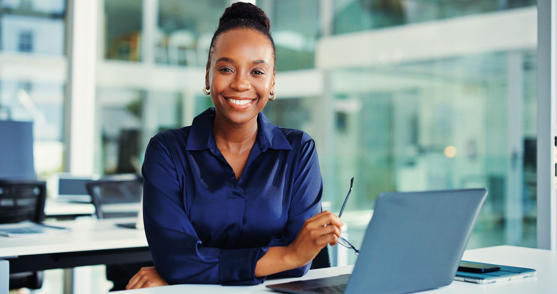 Smiling professional seated at a desk using a laptop in a bright office