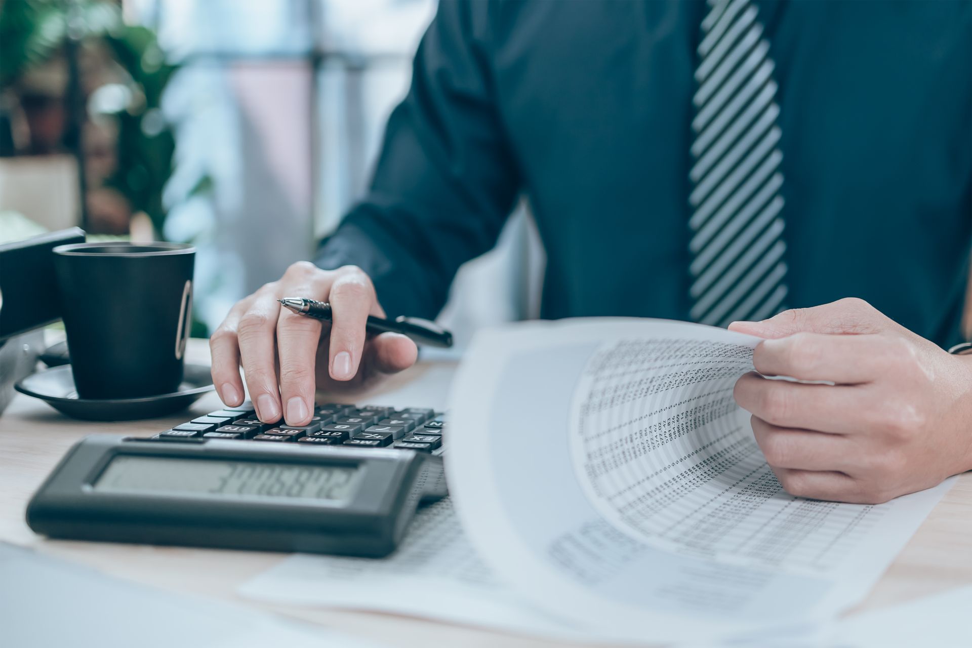Person reviewing papers and using a calculator at a desk with a coffee cup.
