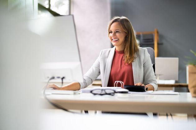 Woman smiling at a desk in a bright office, with a laptop and glasses in the foreground