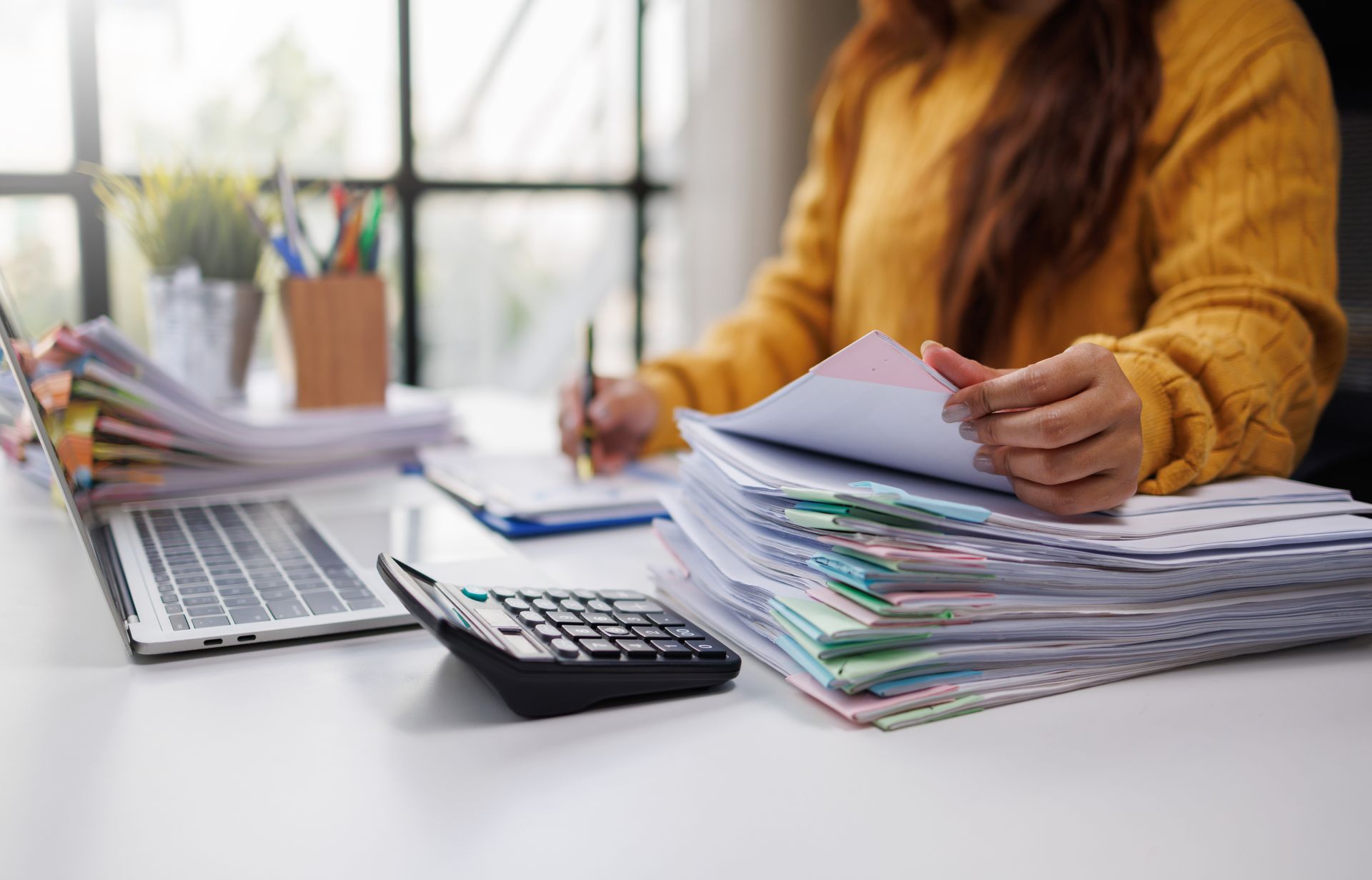 Person sorting paperwork beside a laptop and calculator on a desk
