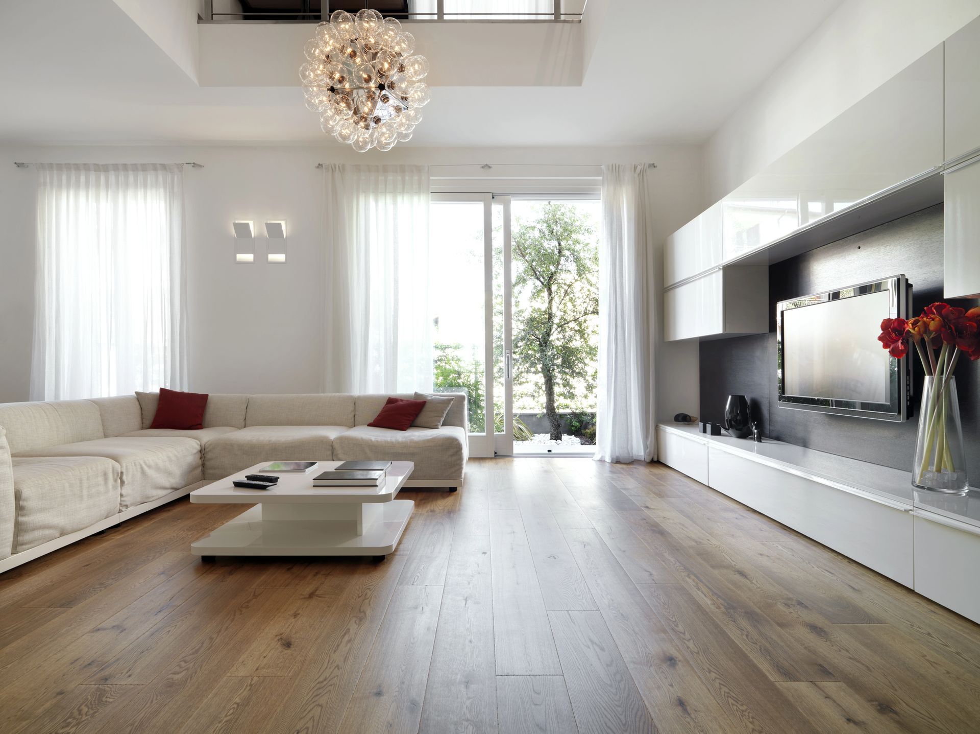 Soggiorno moderno con divano componibile bianco, pavimenti in legno e ampia finestra.