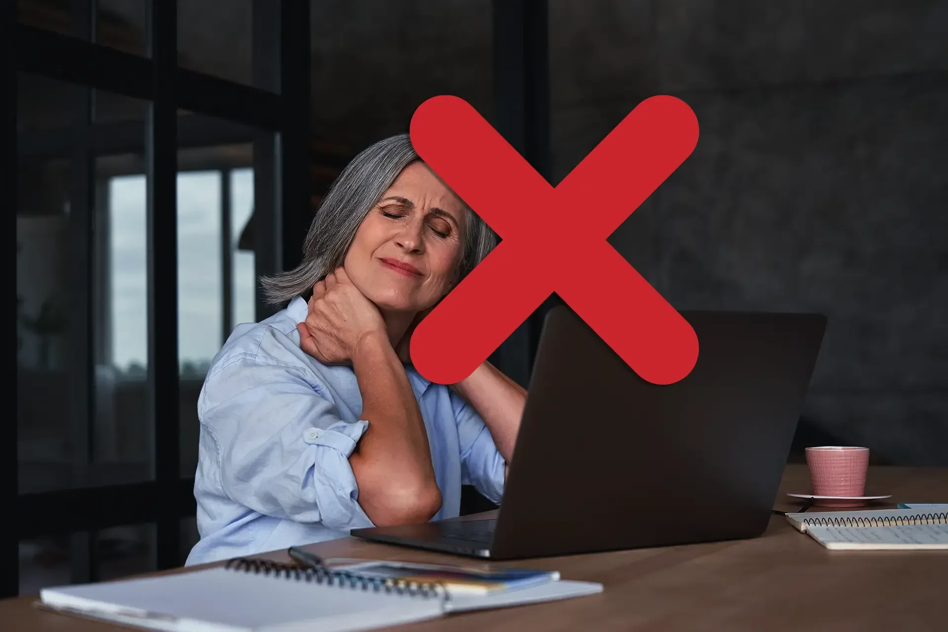 Foto de uma mulher em frente de um laptop, com as mãos massageando a nuca e expressão de dor com um 