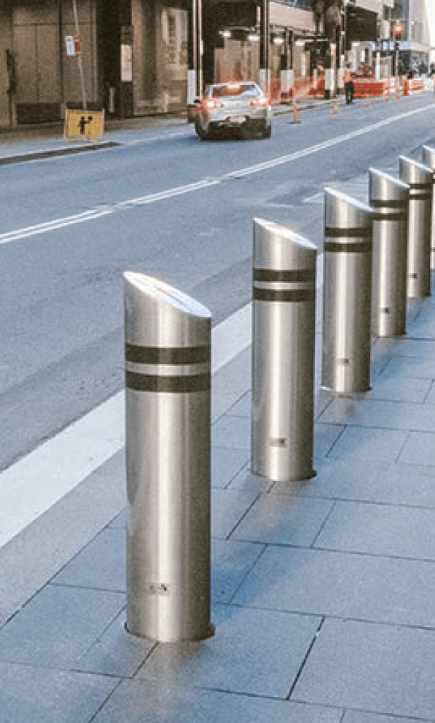 Row of stainless steel bollards along a city sidewalk beside a street