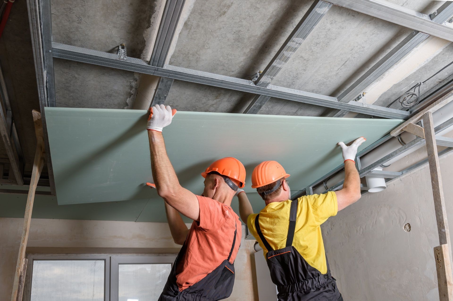 Two construction workers are installing a ceiling in a room.