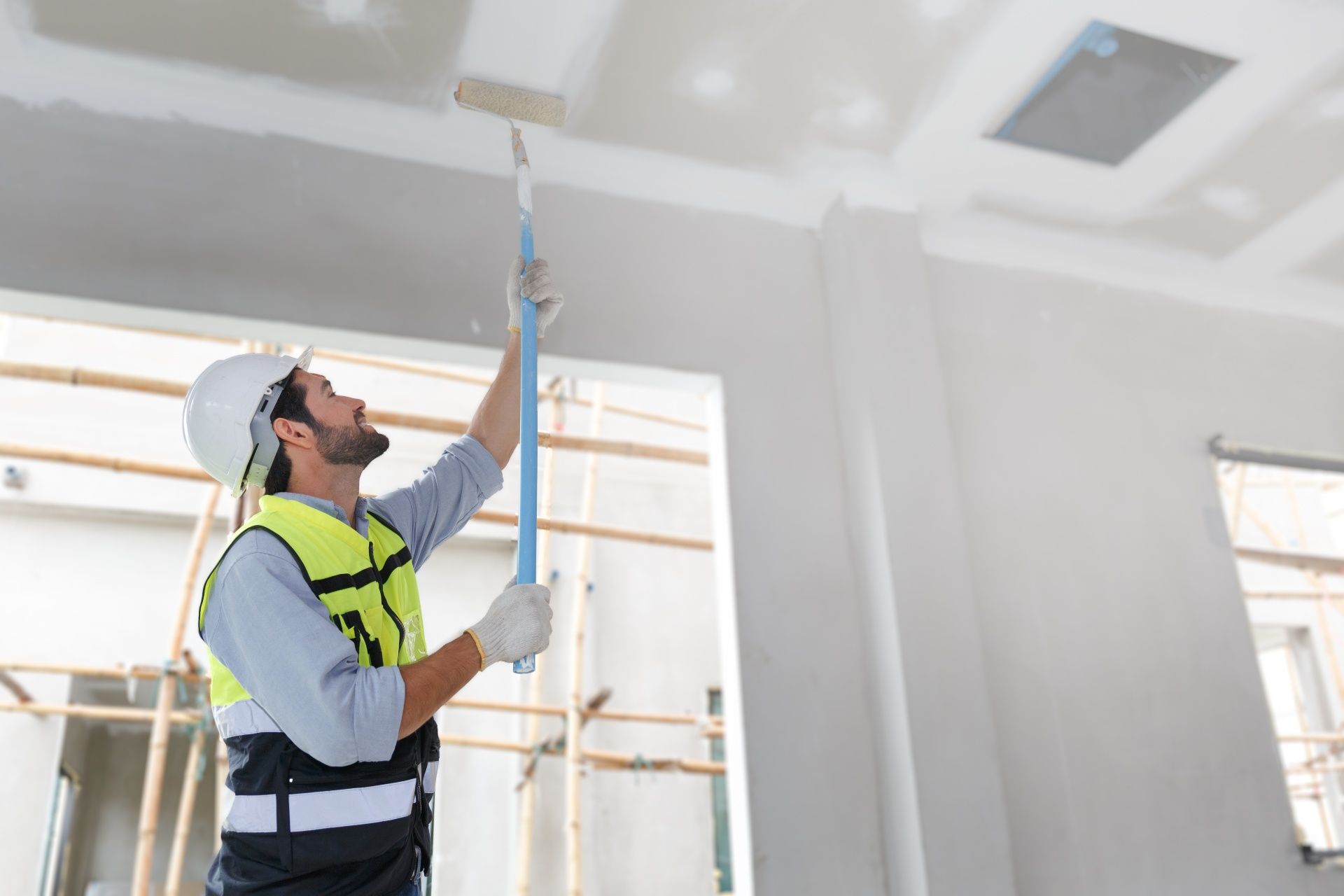 A man is painting the ceiling of a room with a roller.