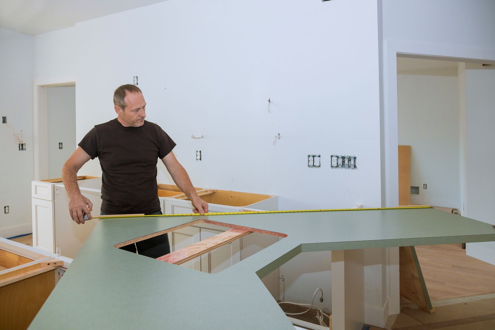 A man is measuring a kitchen counter with a tape measure.
