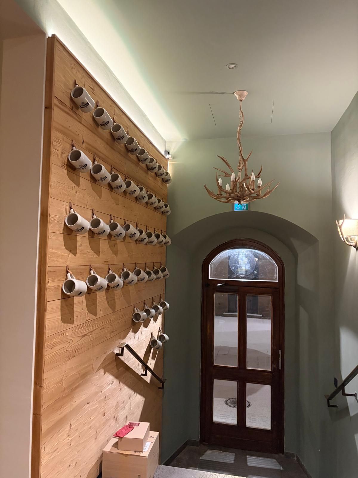 Seiteneingang mit einer Holzverkleidung an der Wand, an der sehr viele Bierkrüge von Tucher hängen.