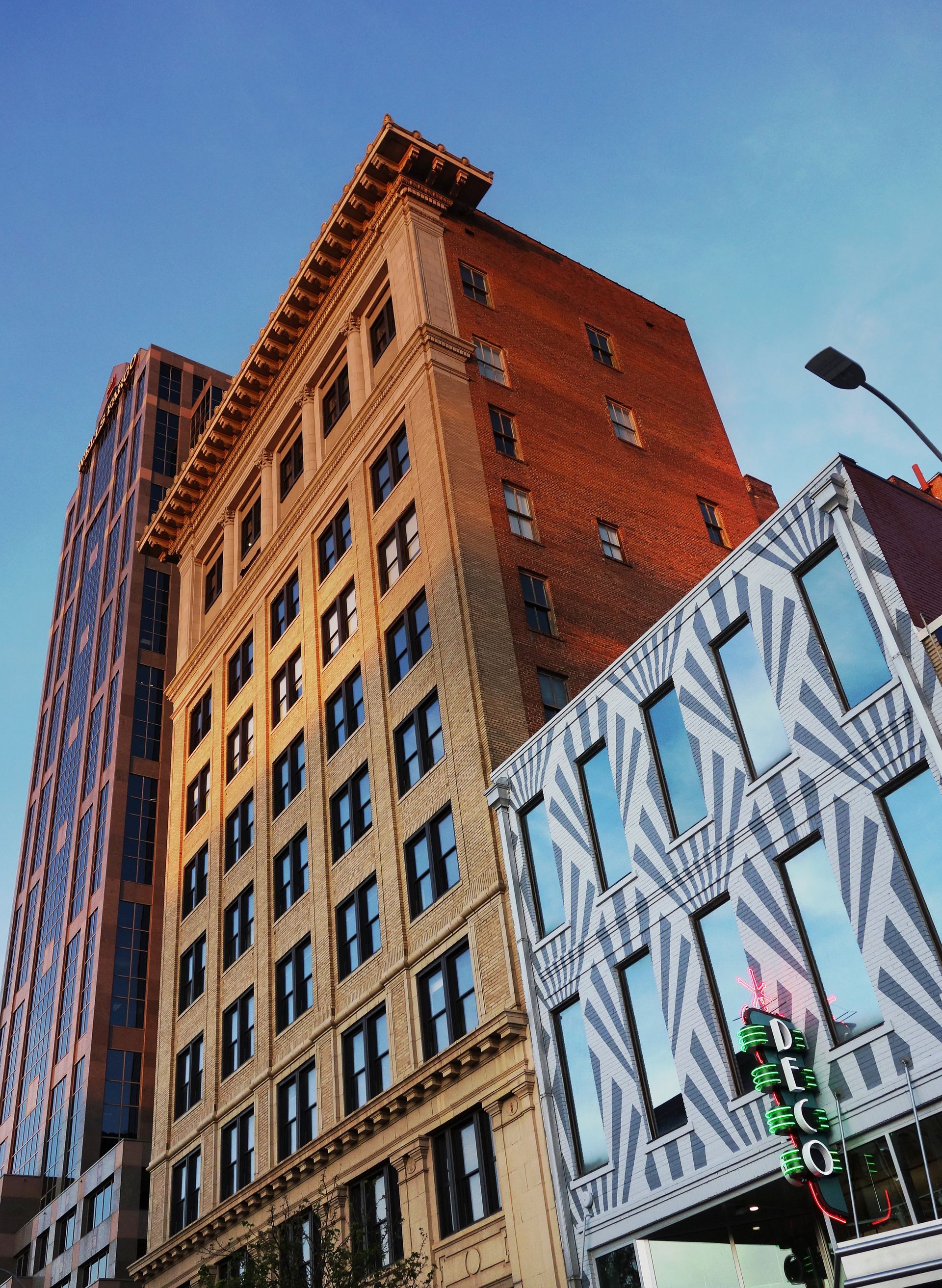 Tall buildings in downtown area: brick, beige, and patterned facade under a blue sky.