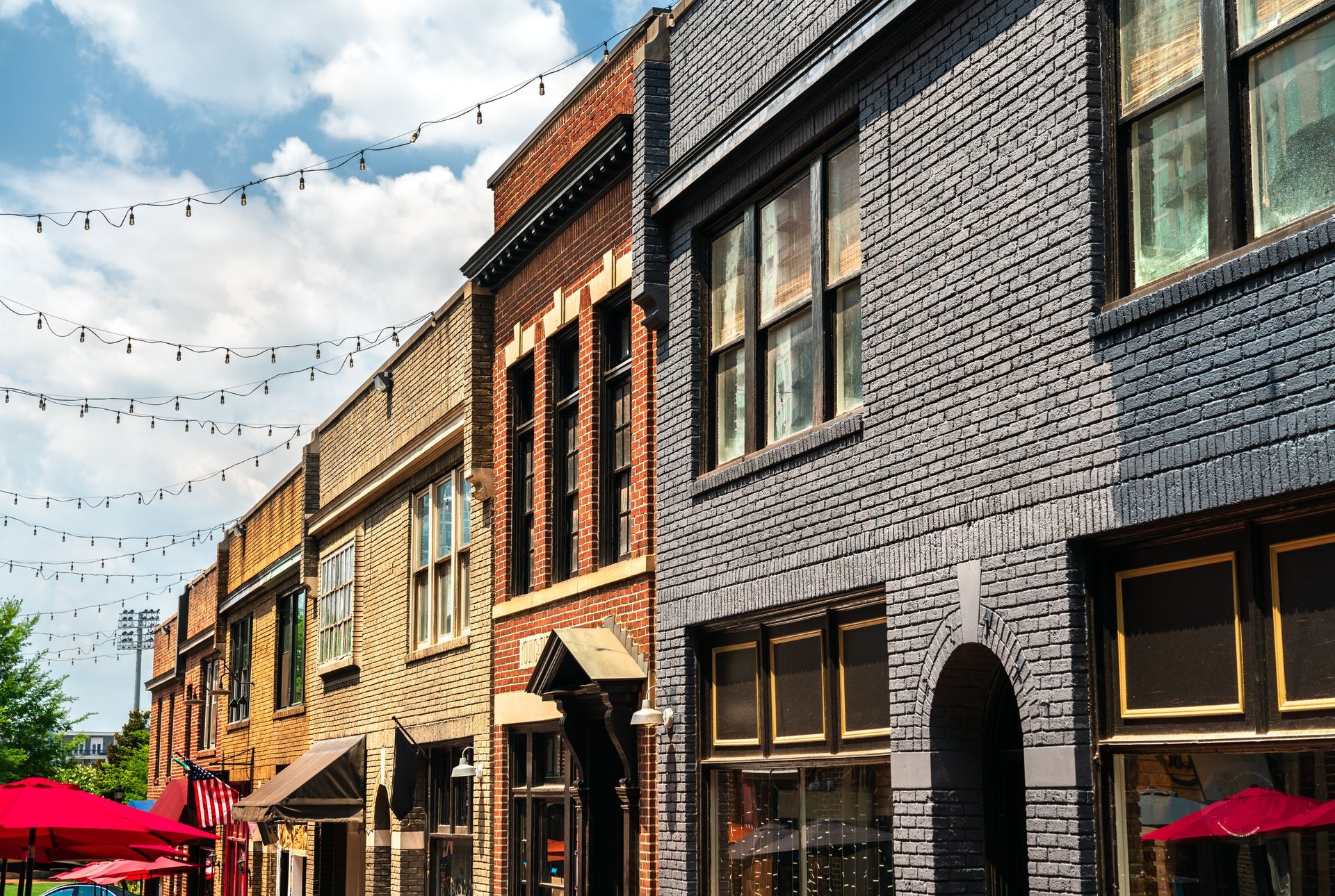 Row of brick buildings with string lights, cloudy sky.