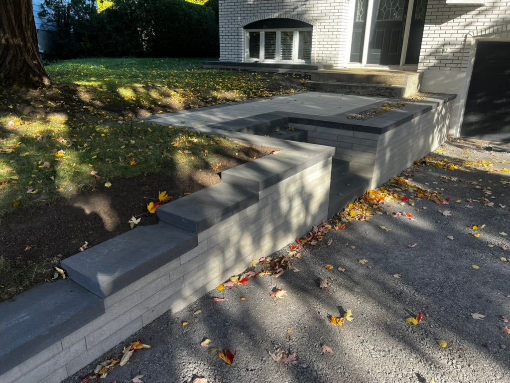 Mur de soutènement en briques grises avec marches menant à l'entrée d'une maison ; feuilles d'automne au sol.